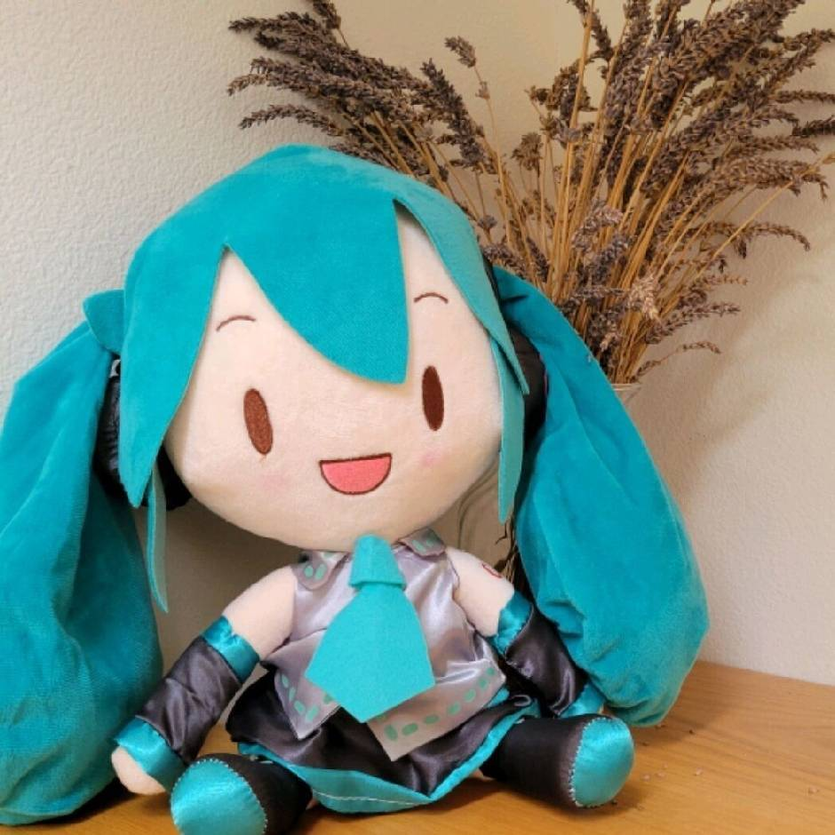 A smiling Hatsune Miku plush sitting in front of dried flowers